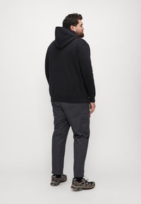 Schwarzer Kapuzenpullover mit lockerer Passform, kombiniert mit dunkelgrauen Cargo-Hosen mit Taschen. Getragen mit schwarzen und grauen Sportschuhen.