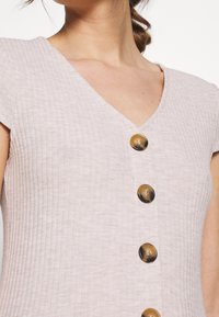 Vestito rosa chiaro a coste con scollo a V e cinque bottoni marroni sul davanti. Maniche corte a cappuccio e tessuto liscio.