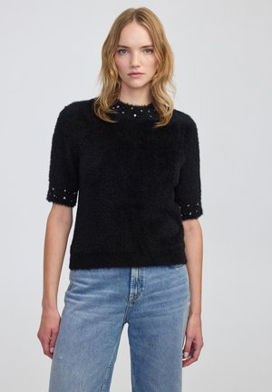 Czarny puszysty sweter z krótkimi rękawami, ozdobiony koralikowym dekoltem. Materiał ma miękką teksturę, zestawiony z jasnoniebieskimi dżinsami.