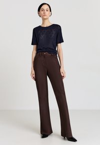 Maglia a maglia con motivo navale e maniche corte abbinata a pantaloni a vita alta, larghi e marroni. I pantaloni presentano un bottone frontale e tasche.