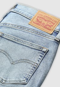 Lichtblauwe spijkerbroek met een gestructureerde afwerking, voorzien van een bruin leren label met rode opdruk, zichtbare stikseldetails op de achterzak.