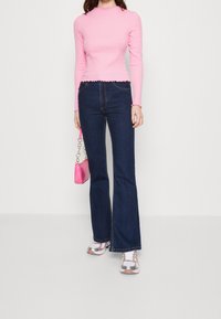 Ljusrosa långärmad topp med scallop-kant, tillsammans med mörkblå utsvängda jeans, rosa handväska och silverfärgade sneakers.