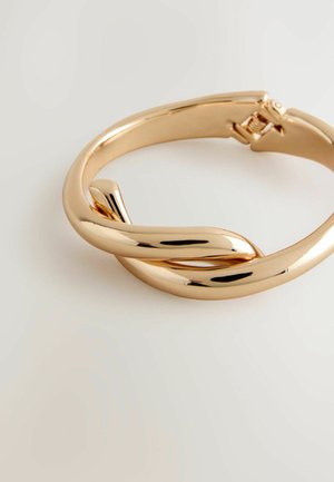 Kullanılan metal altın tonlarında, şık bir pürüzsüz yüzeye sahip ve güvenli bir toka kapanışına sahip kıvrımlı tasarımlı bir bilezik.