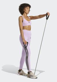 Completo di reggiseno sportivo e leggings in leggero lavanda con dettagli neri. Il modello tiene una banda elastica. Le scarpe da ginnastica presentano un design beige e nero.