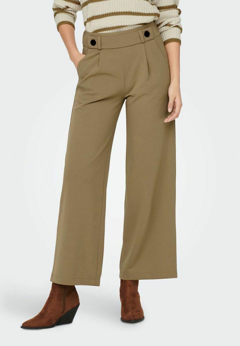 Khaki wijdvallende broeken met een hoge taille, plooien en decoratieve zwarte knopen. Gepaard met een paar bruin suède enkellaarsjes. Glad textuur.