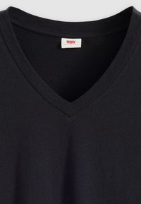 Tricou negru cu decolteu în V, din bumbac. Prezintă o textură moale și o guler cusut. Eticheta Levi's vizibilă la mijlocul gulerului.