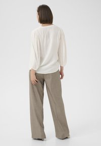 Blusa de color claro con puntos texturizados, mangas abullonadas y escote redondeado, combinada con pantalones de tiro alto y pierna ancha en color beige.