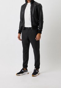 Chaqueta bomber de cuero negra, camiseta blanca, pantalones oscuros y zapatillas negras con detalles blancos y suelas de goma. Incluye puños y cintura acanalados.