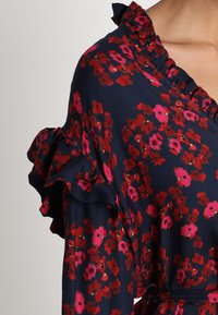 Vestido floral de color azul marino con un escote y detalles de mangas con volantes. Presenta patrones florales rojos y rosas sobre un fondo oscuro. Tejido suave.