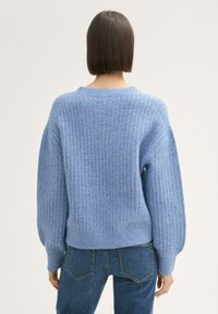 Blauer Strickpullover mit strukturiertem Muster, weiten Ärmeln und geripptem Saum. Getragen mit blauen Jeans, von hinten betrachtet.