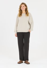 Hellgrauer Sweatshirt mit elastischen Bündchen und Saum, kombiniert mit schwarzen, lockeren Hosen. Braune Slipper vervollständigen das Outfit.