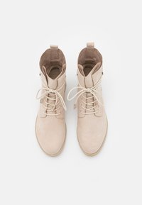 Botines de ante beige con cordones atados en lazo, punta redonda y lengüetas en la parte posterior, mostrados desde una vista vertical en un fondo blanco.