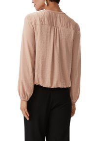 Jasnoróżowa bluzka z długim rękawem, z marszczonym tyłem, elastycznymi mankietami i lekko luźnym krojem, wykonana z miękkiego, teksturowanego materiału.