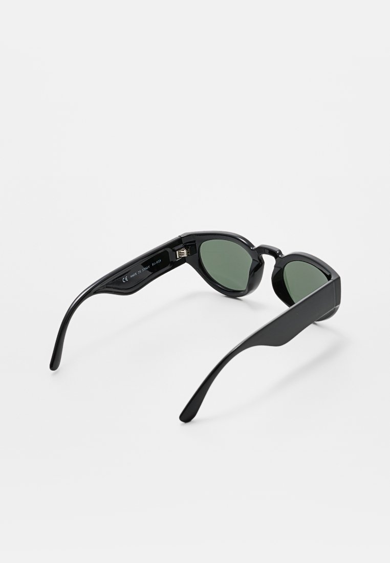 Lunettes de soleil noires avec des verres ronds, teinte verte et monture élégante. Comprend un port de charge sur le côté intérieur de la branche.
