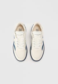 Baskets de sport blanches et marines avec cuir perforé, lacets plats et semelle en caoutchouc. Logo de la marque visible sur la languette.