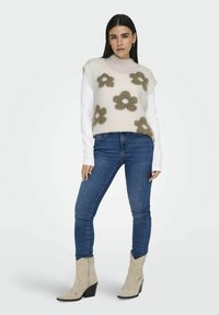 Hellrosa gestrickter Pullover mit floralen Design in Beige; über einem weißen Langarmshirt getragen. Kombiniert mit blauen Skinny-Jeans und beigen Ankle Boots.