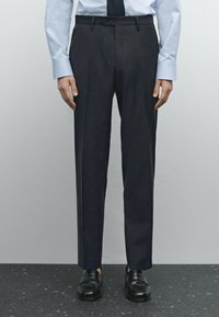 Donkergrijze op maat gemaakte broek met een slim fit, riemlussen en een vlakke voorkant, gecombineerd met zwarte schoenen en een lichtblauw shirt.