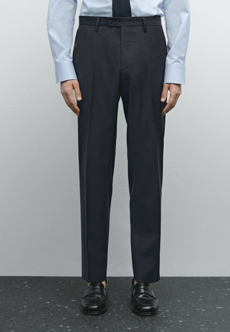 Donkergrijze op maat gemaakte broek met een slim fit, riemlussen en een vlakke voorkant, gecombineerd met zwarte schoenen en een lichtblauw shirt.