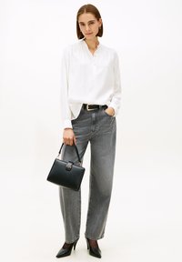 Blusa blanca de manga larga con cuello abotonado, combinada con jeans grises de talle alto. Accesorios incluyen un bolso pequeño negro y tacones puntiagudos.