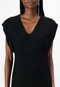 Black, textured dress with a V-neckline and short flutter sleeves. The design features a fitted waistband and flowing silhouette.