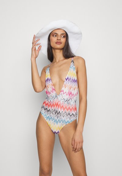 Jednodijelni kupaći kostim s oblikom cik-cak u više boja, dubokim V-izrezom i tankim naramenicama. Uparen s bijelim šeširom širokog dijela.