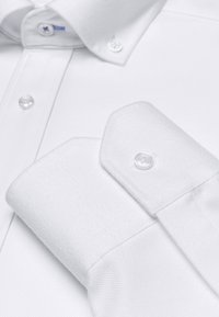 Chemise blanche avec un tissu texturé, col button-down et boutons lisses. Elle possède un poignet simple et anglé avec un bouton.