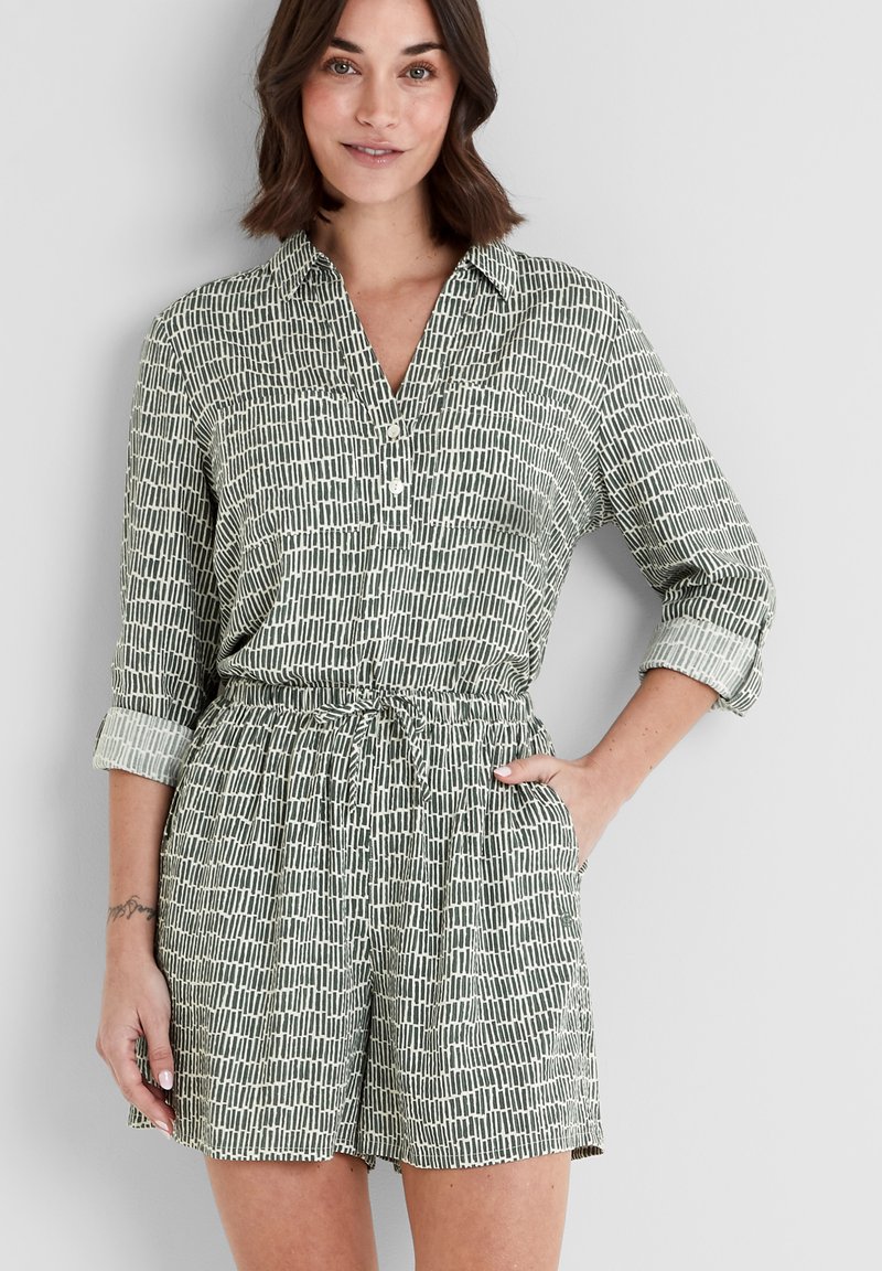 Short-sleeve, olive-green jumpsuit with a collar, featuring a geometric white print, elastic waist, and side pockets. Smooth fabric texture.