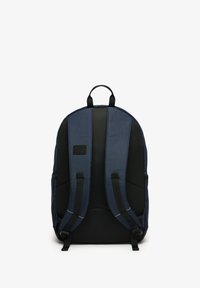 Marineblå rygsæk med polstrede, netstrukturerede rygstropper, en tekstureret overflade, logo-patch og sorte accenter. Har et topgreb til at bære med.