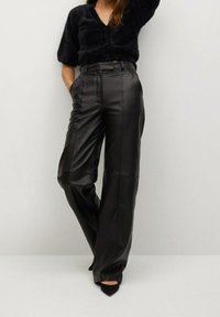 Pantaloni in pelle nera a gamba larga con vita alta, cuciture dettagliate e una texture liscia. Abbinati a un top nero texturizzato e tacchi a punta.