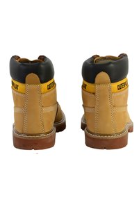 Bottes de travail en cuir tan avec un col rembourré noir, un branding jaune, des coutures renforcées et des semelles en caoutchouc ; conception de hauteur au niveau de la cheville.