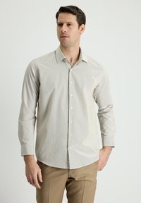 Camicia grigio chiaro con una sottile texture a righe, maniche lunghe, colletto a punta e bottoni bianchi, abbinata a pantaloni beige.