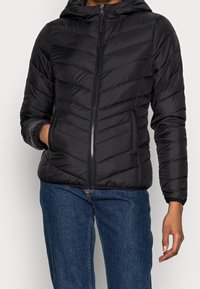 Černá péřová bunda s kapucí, se zipem vpředu, prošitím ve tvaru rybí kosti a bočními kapsami, doplněná modrými džínami.