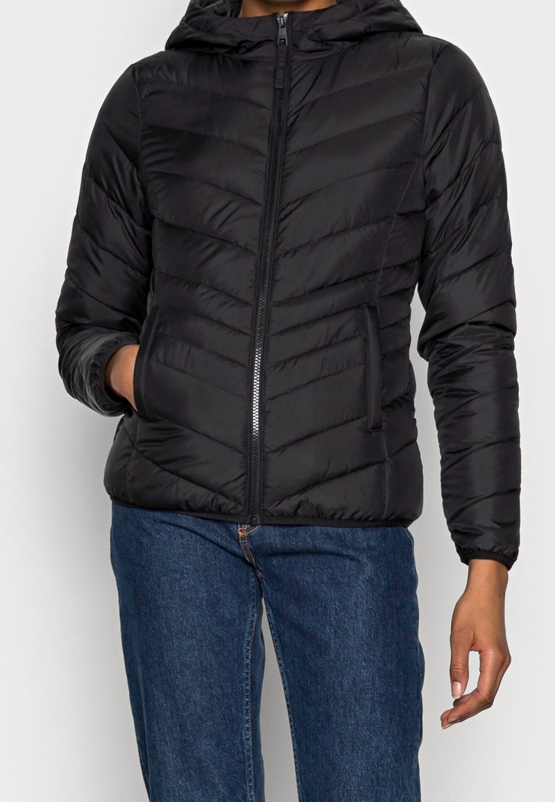 Černá péřová bunda s kapucí, se zipem vpředu, prošitím ve tvaru rybí kosti a bočními kapsami, doplněná modrými džínami.