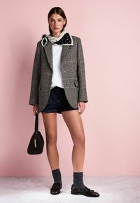 Žaketas su šachmatų raštu, struktūruoto silueto, uždėtas ant balto marškinėlio, suderintas su tamsiomis džinsų šortais, pilkomis kojinėmis ir blizgiais rudiems loaferiais.