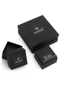 Des boîtes noires en papier recyclé avec le logo "Kuzzoi", de différentes tailles, arborant une texture mate et un design minimaliste. Des étiquettes indiquent des matériaux écologiques.