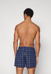 Marinefarbene Badehose mit einem karierten Muster in Hellblau und Orange. Hergestellt aus leichtem Stoff mit elastischem Bund für zusätzlichen Komfort.
