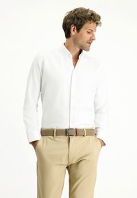 Camicia bianca con bottoni e maniche lunghe, abbinata a pantaloni beige e una cintura intrecciata color beige. Texture morbida e vestibilità sartoriale.