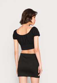 Top preto cropped com mangas bufantes, apresentando um decote arredondado e detalhes franzidos. Combinado com uma saia mini preta a condizer.