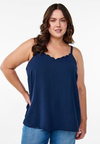 Top sin mangas de color azul marino con escote en forma de concha, fabricado en tejido ligero, de corte relajado, combinado con jeans de mezclilla azules.