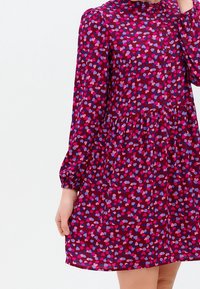 Sukienka krótki rękaw w głębokim burgundzie z wzorem serc w różowym i niebieskim. Posiada zapięcie na guziki z przodu i elastyczne mankiety.