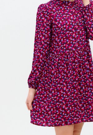 Lyhythihainen mekko syvän burgundinvärisenä, jossa on sydänkuvio vaaleanpunaisena ja sinisenä. Mekossa on napitettava etuosa ja joustavat hihansuut.