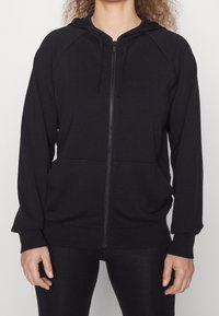 Sudadera con cremallera negra, con cierre frontal, capucha ajustable con cordón y bolsillos laterales. Fabricada en tejido suave y con un corte relajado.