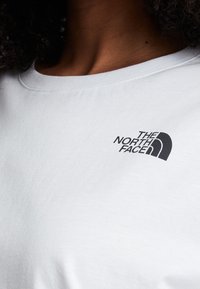 White cotton t-shirt featuring a black graphic logo of "The North Face" on the left chest area. Round neck and short sleeves.