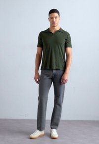 Camisa polo de manga corta verde oscuro, jeans ajustados grises y zapatillas blancas. La tela parece suave con una textura lisa y sin patrones.
