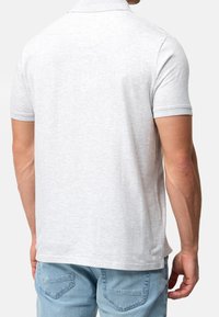 Polo shirt grigio chiaro con maniche corte, colletto classico e texture liscia, che mostra le cuciture e una vestibilità rilassata su un modello.