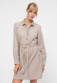 Light beige shirt dress made of textured fabric, featuring a button-up front, collar, long sleeves, and a fabric belt at the waist.
