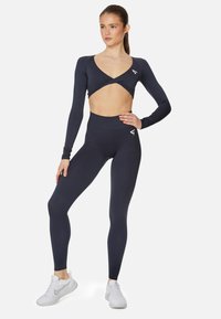 Navy Sportanzug bestehend aus einem langärmligen Crop-Top mit tiefem V-Ausschnitt und hochtaillierten Leggings. Glattes Material mit taillierter Silhouette.