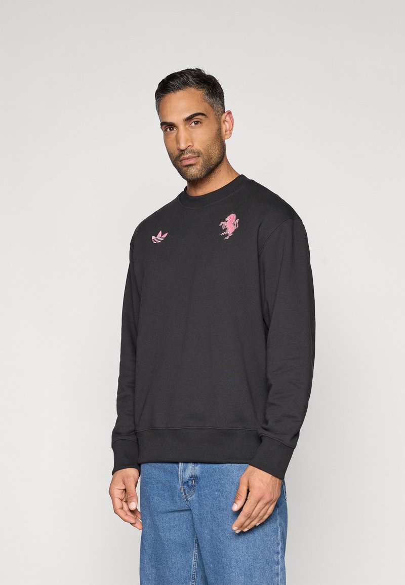 Felpa nera con scollo rotondo, caratterizzata da ricami rosa di un leone e dai loghi trefoil di Adidas. Realizzata in cotone, presenta polsini e orlo a coste.