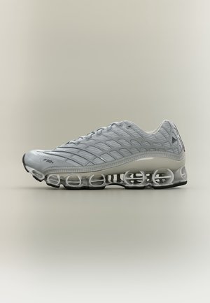 Chaussure de sport Adidas grise avec empeigne en mesh, marquage F50+ et semelle translucide semblable à un ressort, conçue pour l'amorti et le maintien.