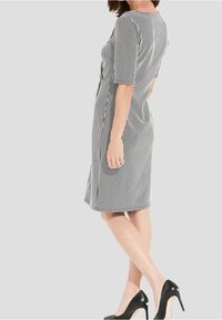 Gestreiftes Kleid in Schwarz und Weiß, taillierte Passform, knielang, mit kurzen Ärmeln und einem seitlichen Schlitz, kombiniert mit schwarzen High Heels.